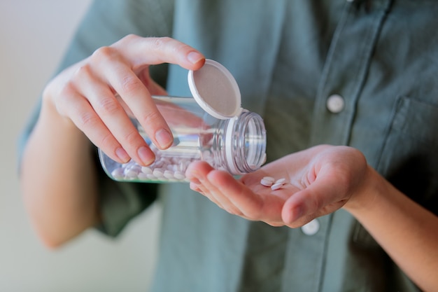 Woman pours white pills from a transparent jar into her hand.