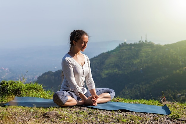 Woman practices yoga asana Baddha Konasana bound angle pose outdoors in Himalayas mountains