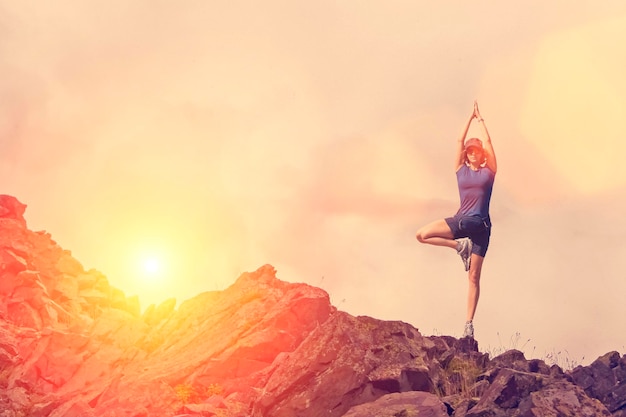 A woman practices yoga on a background of mountains and sky\
toned