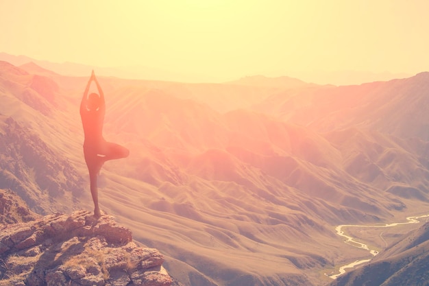 A woman practices yoga on a background of mountains and\
sky