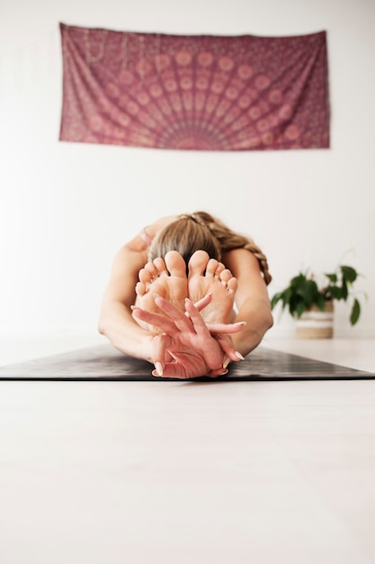 A woman practices yoga she is bent on the floor holding her\
feet with her hands in gyan mudra