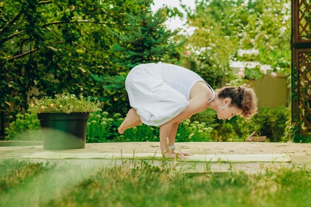 La donna pratica lo yoga nel giardino estivo kakasana crow pose con le braccia piegate