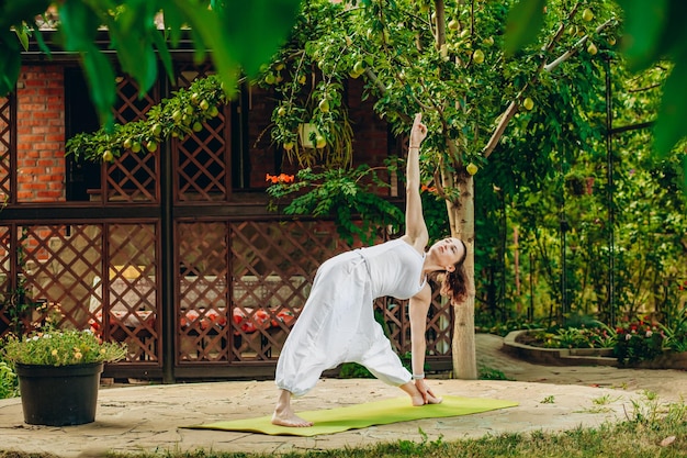 Woman practices yoga in summer garden Utthita Trikonasana Elongated Triangle pose