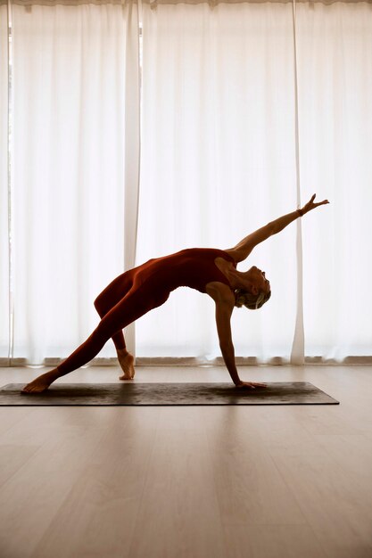 A woman practices yoga in a white room she is in rock star pose