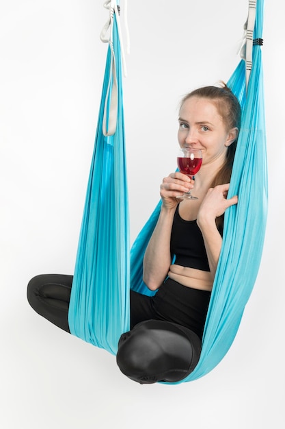 Woman practicing drunk yoga Woman in hammock practicing yoga and holding glass of wine Alcohol or sport