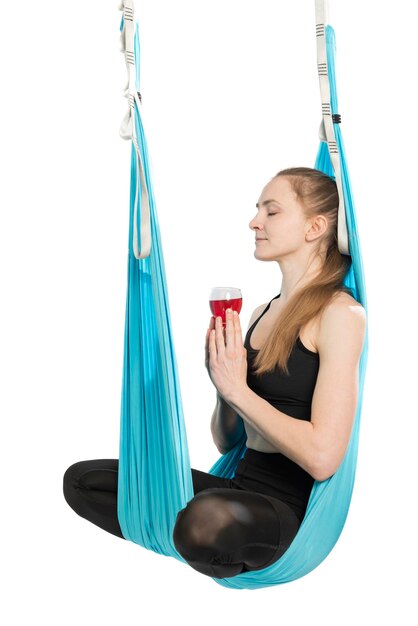 Woman practicing drunk yoga Woman sitting on hammock practicing yoga position holding glass of wine Side view White background