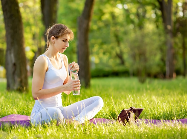 Женщина практикует фитнес и держит бутылку воды на коврик для йоги