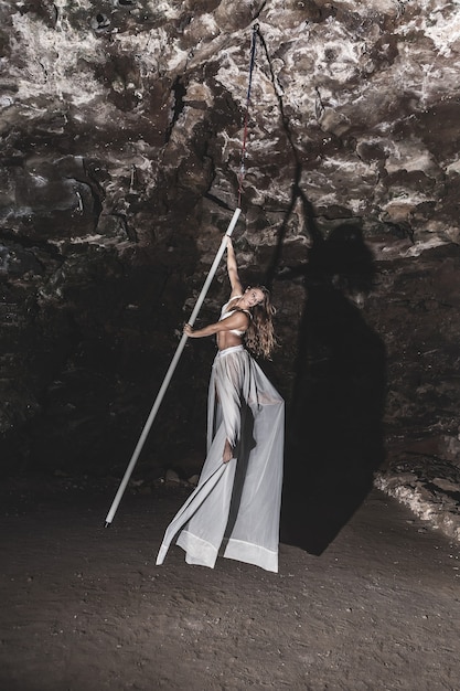 Woman practicing pole dance air in the cave interior