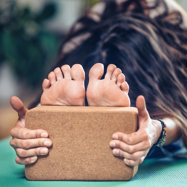 Woman practicing seated forward bend yoga position using yoga blocks on turquoise yoga mat at home