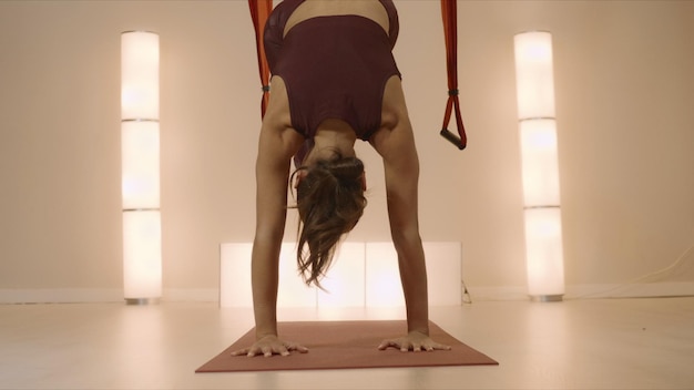 Woman practicing yoga in aero yoga studio Yoga trainer standing on hands at mat