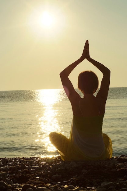 Woman practicing yoga on the beach at sunset.