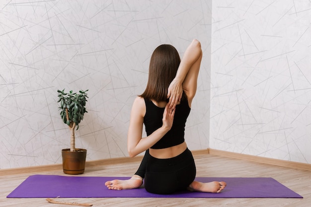 woman practicing yoga in Cow Face Gomukhasana pose while sitting on mat