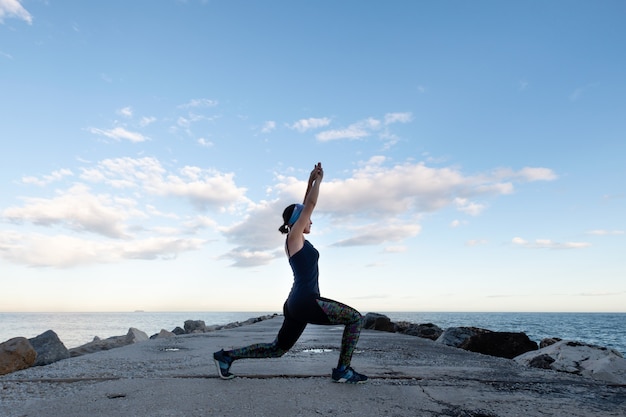 Woman practicing yoga facing the sea on a cloudy day