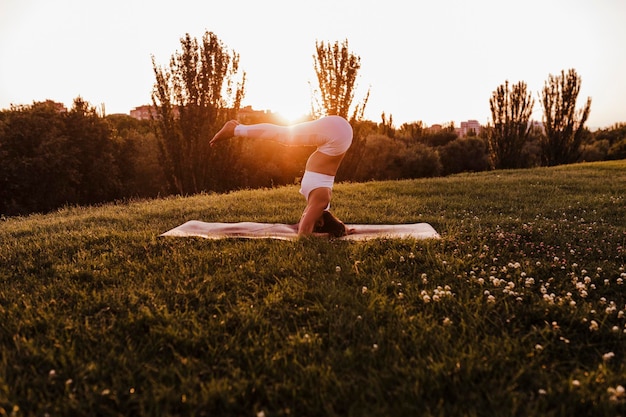 Foto donna che pratica lo yoga sul campo contro un cielo limpido durante il tramonto