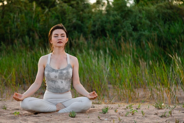 Woman practicing yoga outside in lotus pose on sand