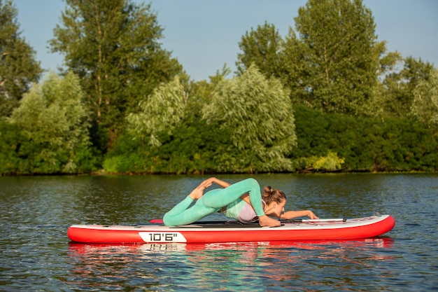 Donna che pratica yoga sulla tavola da paddle al mattino