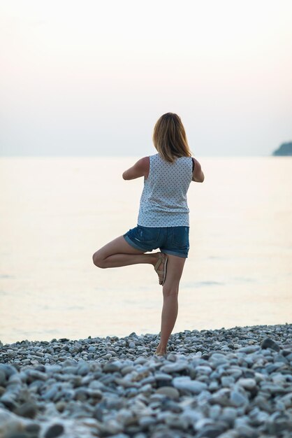 A woman practicing yoga performs vrikshasana exercise on the seashore tree pose