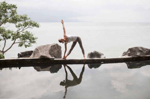 Woman practicing yoga pose in front of the lake at sunrise.