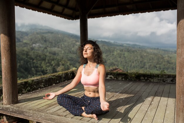 Woman practicing yoga in the traditional balinesse gazebo.