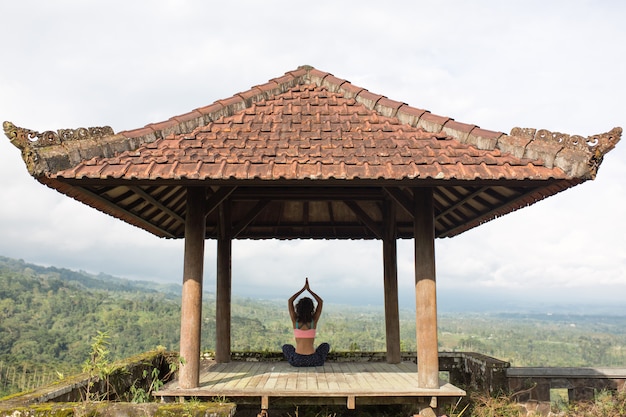 Woman practicing yoga in the traditional balinesse gazebo.