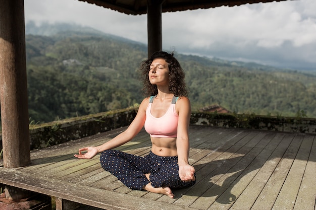 Woman practicing yoga in the traditional balinesse gazebo.