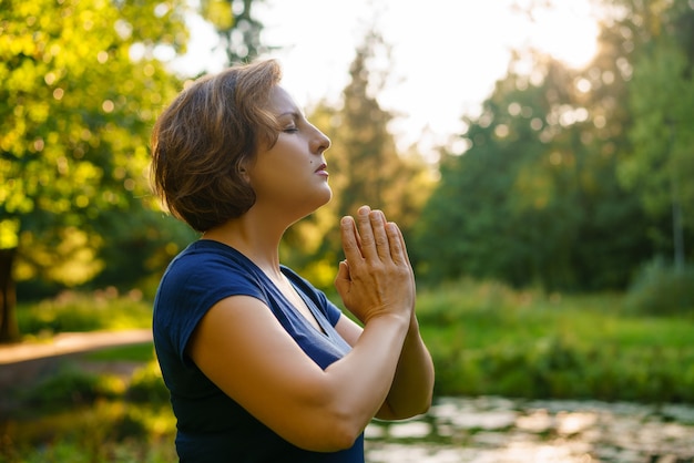 Woman in prayer in nature at sunset in the park