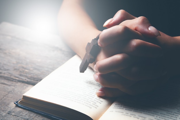 Woman praying on book holding cross