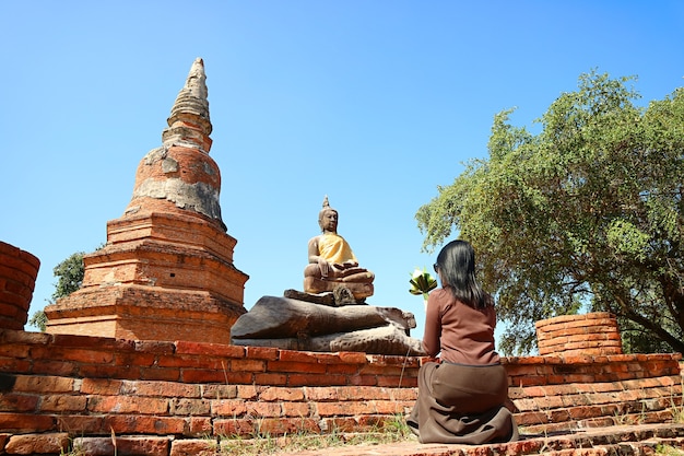 Woman praying in front of buddha image at wat phra ngam temple ruins in thailand