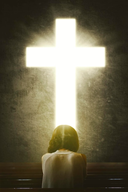 Woman praying to GOD in the front of a bright Cross