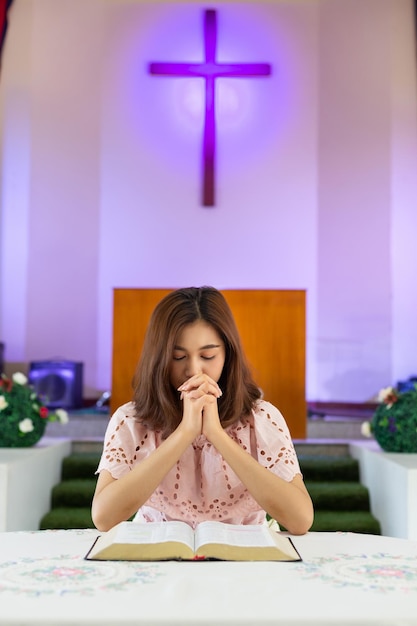 Woman praying with bible while sitting at table in church