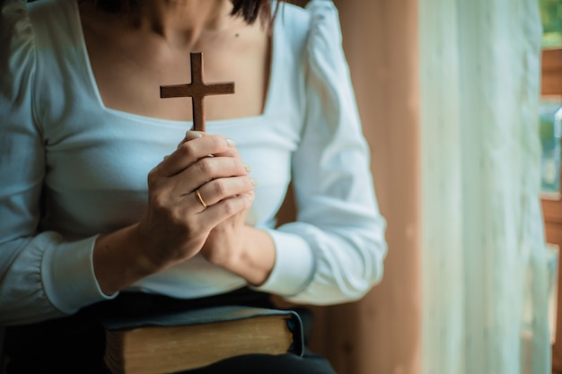 女性は聖書と木製の十字架で祈っています。