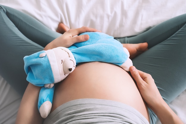 woman pregnant belly with teddy toy bear concept of maternity parenting pregnancy