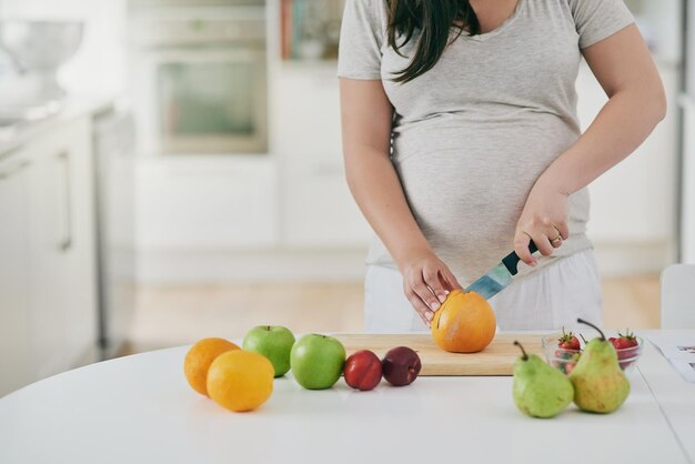 woman pregnant and cutting fruit in home nutrition and vitamin for growth of baby female person organic and vegan snack or hands for health cooking and healthy diet for maternity in kitchen