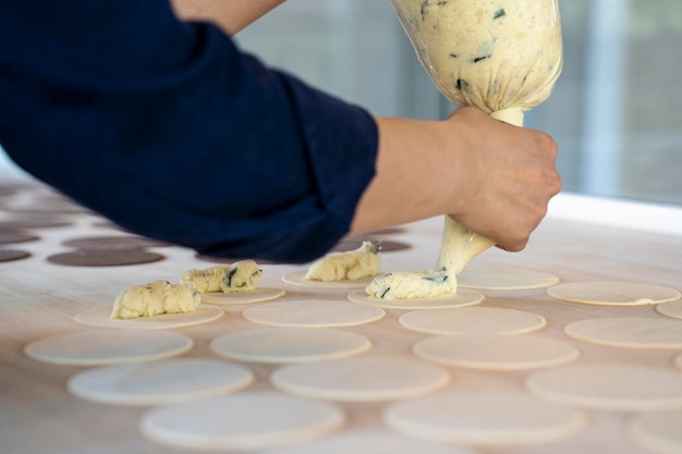 Woman prepare fresh made ravioli inside pasta factory Using a pastry bag or sac a poche to make stuffed pasta ravioli culurgiones agnolotti Focus on stuffed