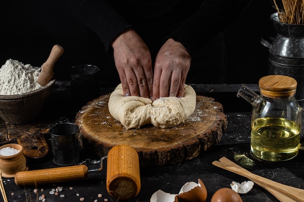 A woman prepares the dough on a dark table. Flour, yeast dough, dark background