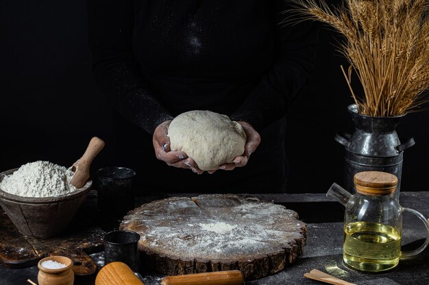 A woman prepares the dough on a dark table. Flour, yeast dough, dark background