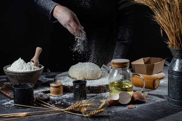 A woman prepares the dough on a dark table. Flour, yeast dough, dark background