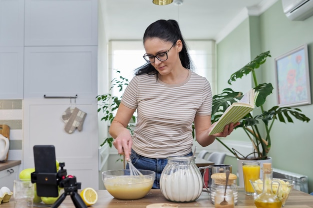 Woman preparing apple pie at home in kitchen talking online using video call