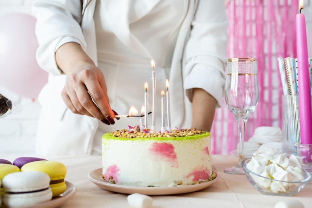 写真 女性がケーキケーキポップマカロンその他の子で誕生日のテーブルを準備しろうそくを点灯しています