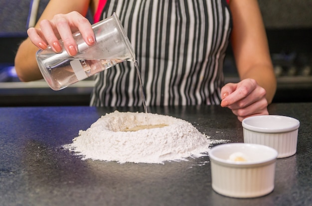 Woman preparing pizza dough on black granite table