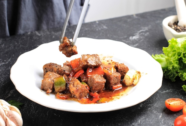 A Woman Preparing Served Korean Black Pepper Bulgogi Beef with Paprika and Kimchi on the Background. Served on White Plate, Black Background. Made from Wagyu Dice Saikoro Beef