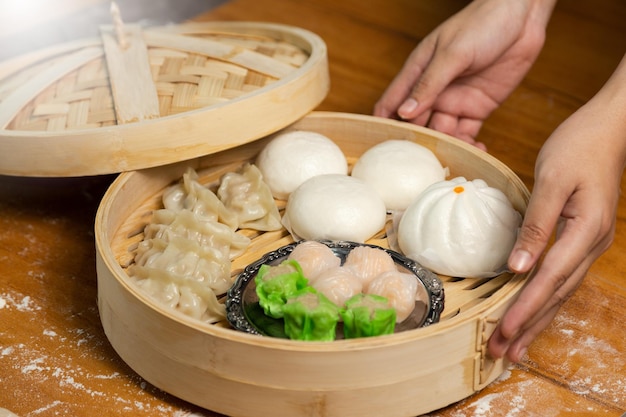 Woman presenting dim sum dumplings boiled and hot chinese dumplings in wooden steamer