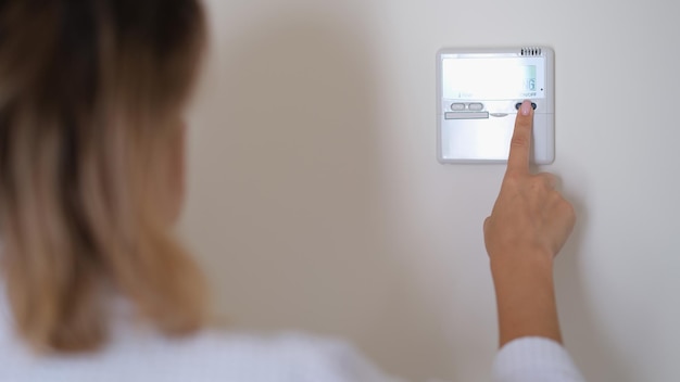 Woman pressing button on remote control of air conditioner in wall closeup