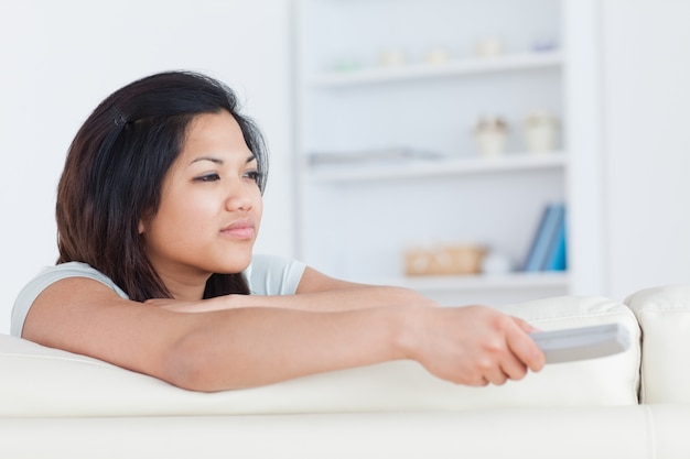 Woman pressing on a television remote while sitting on a white couch