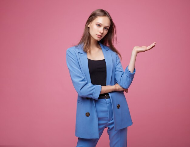 Woman in a pretty blue suit jacket pants posing over pink background Studio shot
