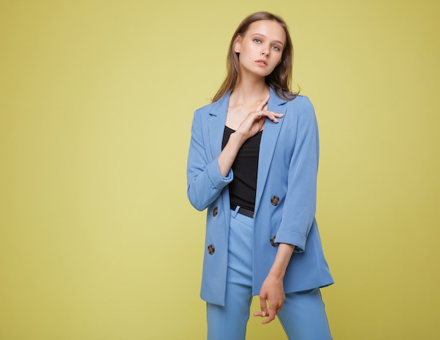 黄色の背景にかわいい青いスーツのジャケットパンツサングラスの女性スタジオショットの肖像画