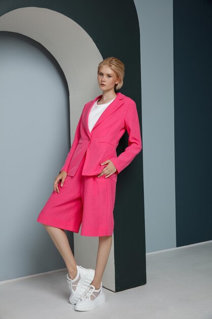 Woman in a pretty pink fuchsia suit jacket blazer shorts posing over textured wall blonde