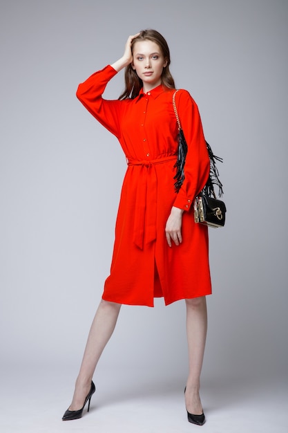 Woman in a pretty red dress black handbag posing over white soft gray background Studio Shot