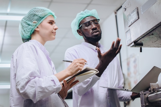 Photo woman production supervisor working with african worker in food factory to checking and report machine problem to engineer in production line.