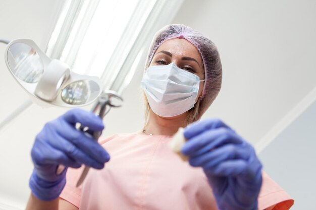 Женщина-профессиональный стоматолог держит форцепс в стоматологическом кабинете, вытаскивает зуб.